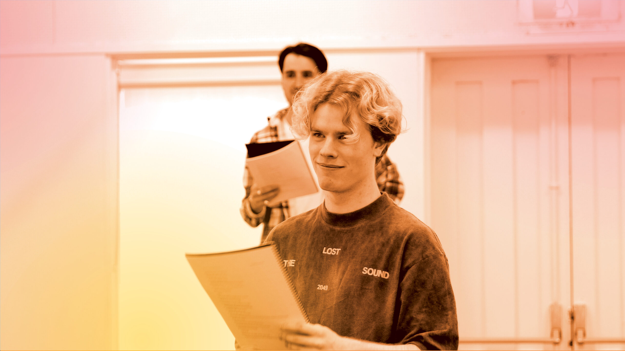 A young actor in rehearsal holds a script and listens to direction.